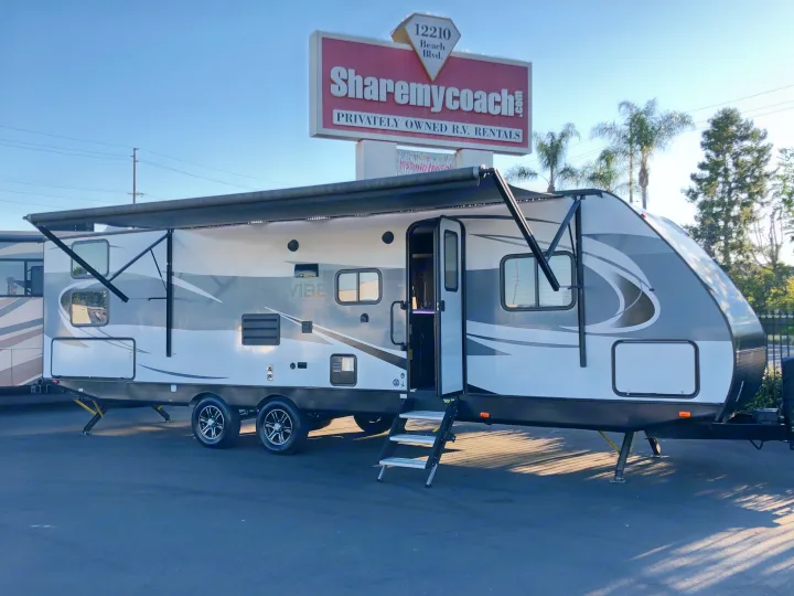 White & gray travel trailer with an extended awning. Available for RV rental from Sharemycoach.com.. Forest River Vibe 2019
