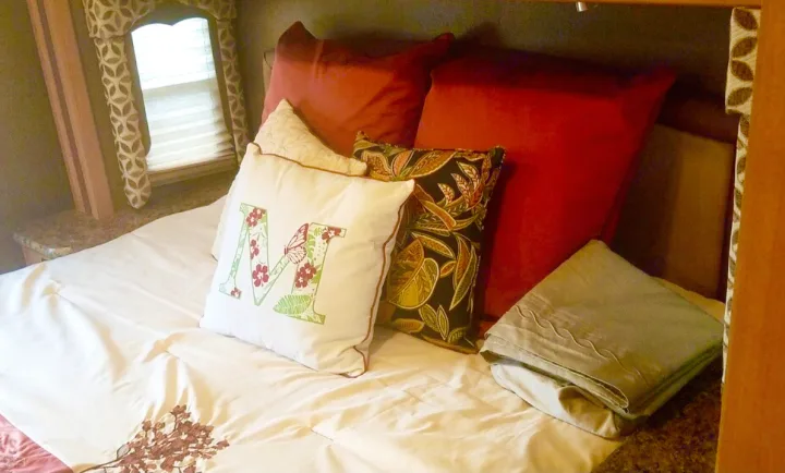 Cozy RV rental bedroom with a comfortable bed and decorative pillows, perfect for a relaxing travel experience.. Other Four Winds 2016