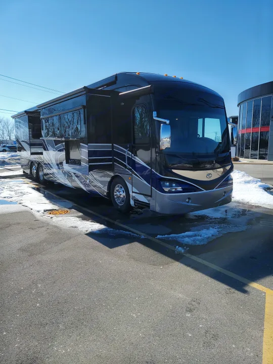 Luxury RV rental motorhome parked outdoors on asphalt with snow patches under clear blue sky.. American Revolution 2019