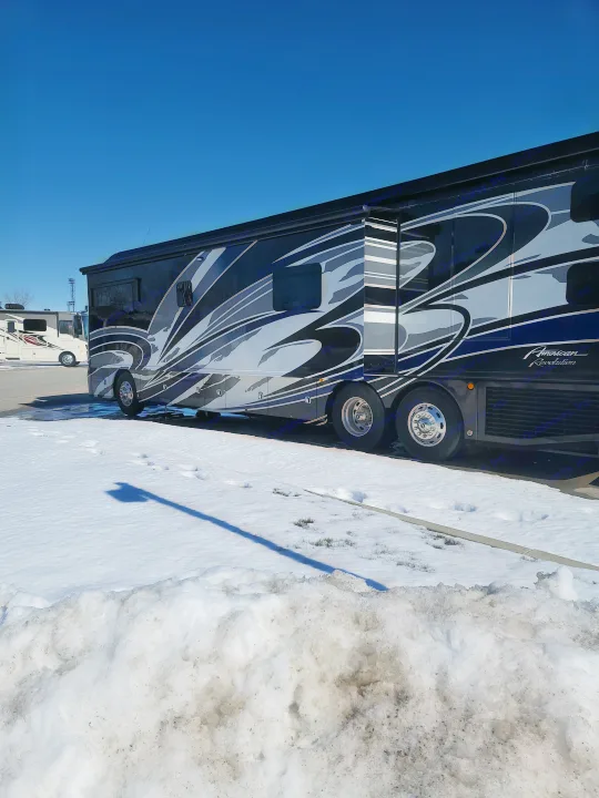 Sleek black luxury RV (motorhome) parked in the snow under a blue sky, perfect for your next rv rental.. American Revolution 2019