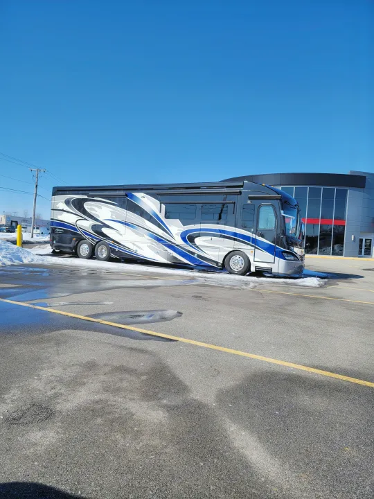 Large, sleek luxury RV with blue/white graphics parked on asphalt. Imagine this stunning RV for your next rental adventure!. American Revolution 2019