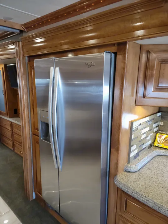 Inside an RV rental, this modern kitchen boasts a large stainless steel Whirlpool refrigerator, wood cabinets, and granite counters.. American Revolution 2019