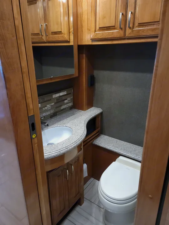 Inside a well-appointed RV rental bathroom, featuring a compact sink, toilet, and light wood cabinetry.. American Revolution 2019