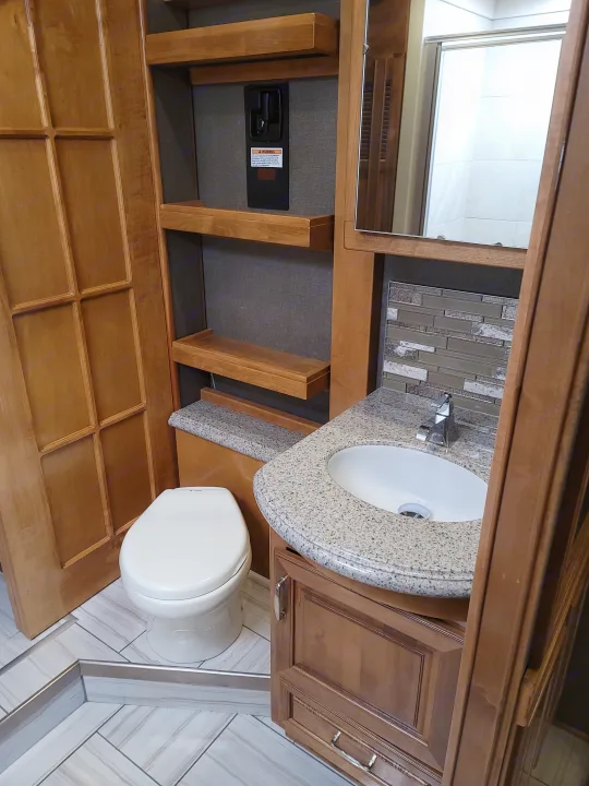 Inside an RV rental, a clean bathroom with modern vanity, sink, toilet, and tiled shower visible in the mirror.. American Revolution 2019