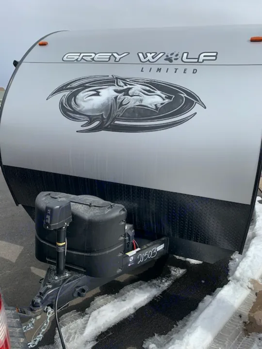 Front view of a Grey Wolf Limited RV, ideal for an RV rental. Shows hitch, battery, and snow-lined ground.. Cherokee Grey Wolf 27DBH 2021