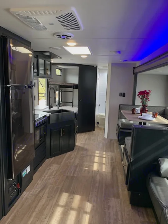 Inside a modern RV rental: living area with couch/TV, full kitchen with appliances, wood-look floor, and a versatile rear space with blue accent lights.. Cherokee Grey Wolf 27DBH 2021