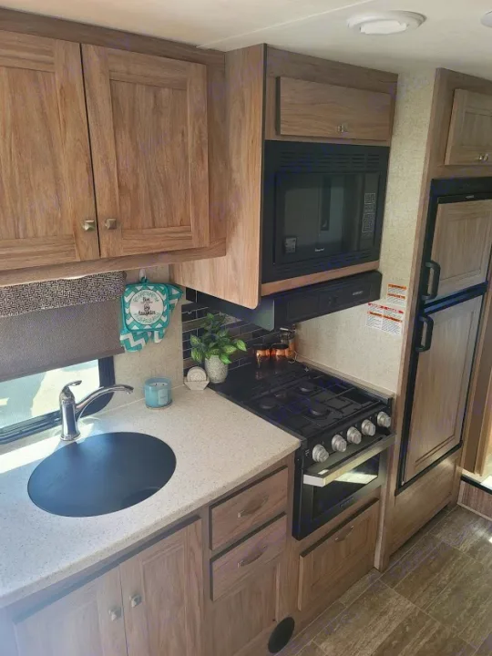 Modern rv rental kitchen featuring a sink, stove, microwave, refrigerator, and ample wood-grain cabinets.. Forest River Sunseeker 2019