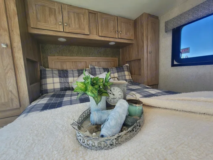 Cozy RV rental bedroom featuring plaid bedding, overhead wood cabinets, and a decorative tray with plants & towels.. Forest River Sunseeker 2019