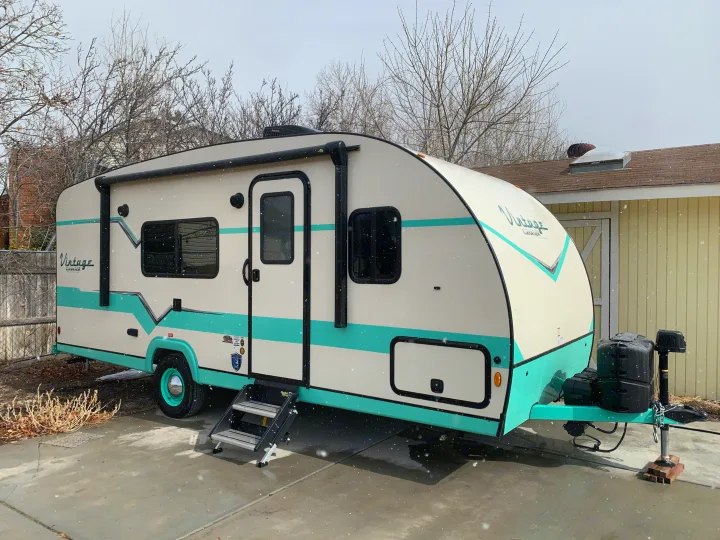 A charming cream and teal Vintage Cruiser travel trailer, ideal for an RV rental, is parked outside in light snow.. Gulf Stream Vista Cruiser 2021