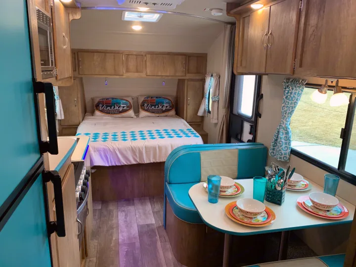 Step inside this charming retro RV rental, showcasing a compact bed, dinette, and kitchen with bright blue accents.. Gulf Stream Vista Cruiser 2021