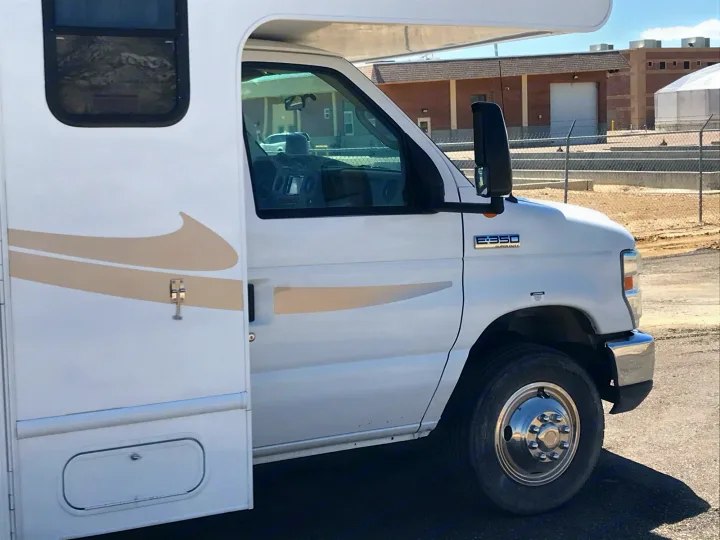 A white Ford E-350 Super Duty rv rental motorhome with beige graphics and an open side door, ready for travel.. Ford Fourwinds 2012