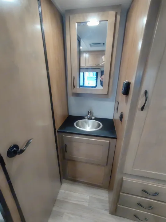 Inside an RV rental: compact bathroom with a vanity, stainless steel sink, mirrored cabinet, and light wood-look floor.. Tiffin Motorhomes wayfarer 2020