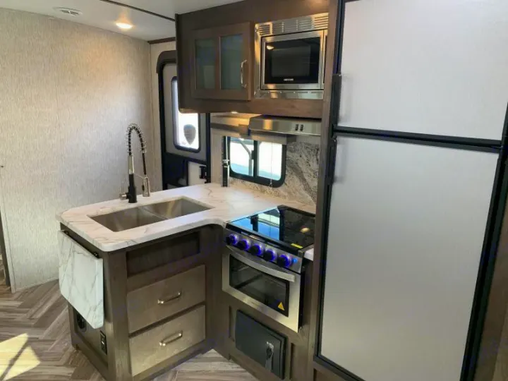 Modern RV rental kitchen with a U-shaped counter, sink, stove, microwave, and full-size fridge, perfect for mobile living.. Dutchmen Denali 2021