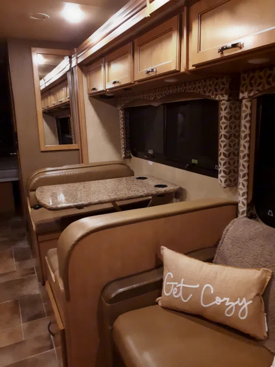 Cozy RV rental dinette area featuring a speckled table with cup holders, plush seating, and overhead cabinets for storage. Get comfy!. Thor Four Winds 2017