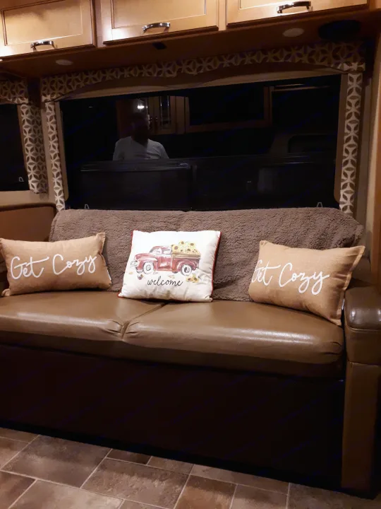 Inside a cozy RV rental: sofa with "Get Cozy" pillows, warm wood cabinets, and large window blinds for privacy.. Thor Four Winds 2017