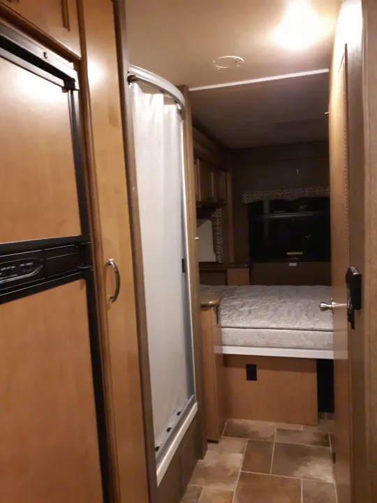 View inside an RV rental showing a refrigerator, compact shower, and a bedroom area with a bed, highlighting the efficient layout.. Thor Four Winds 2017
