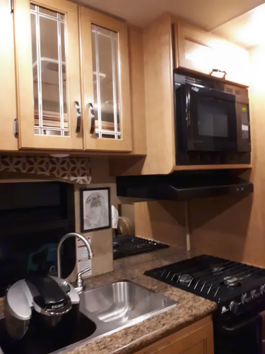 RV rental kitchen view: light wood cabinets, microwave, stovetop, sink, Keurig, providing a compact cooking area.. Thor Four Winds 2017