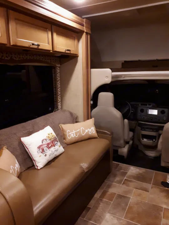 Relax in this cozy RV rental interior, featuring a sofa with a "Get Cozy" pillow, overhead cabinets, and the front cabin.. Thor Four Winds 2017