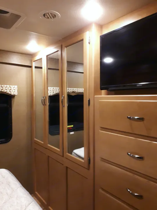 Cozy RV rental bedroom featuring mirrored closet, TV, and ample storage for a comfortable stay.. Thor Four Winds 2017