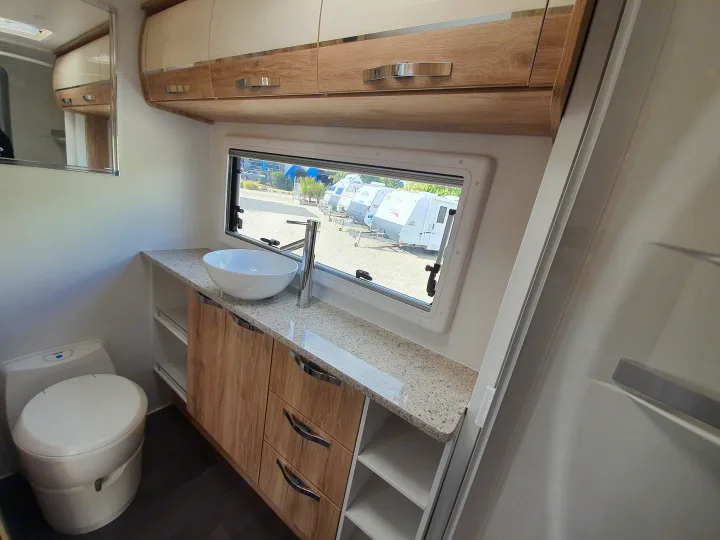 RV rental ensuite: Modern bathroom with toilet, bowl sink, wood cabinetry, and a window view of other RVs.. Avan Aspire 555 2021