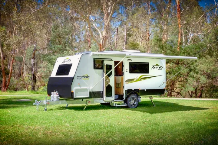 An Avan Aspire caravan, perfect for RV rental, sits on green grass with an extended awning and open door. Tall trees in background.. Avan Aspire 555 2021
