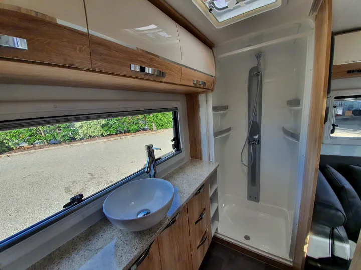 Modern RV rental interior with a spacious shower, vanity with sink, sleek overhead cabinets, and a scenic window view.. Avan Aspire 555 2021