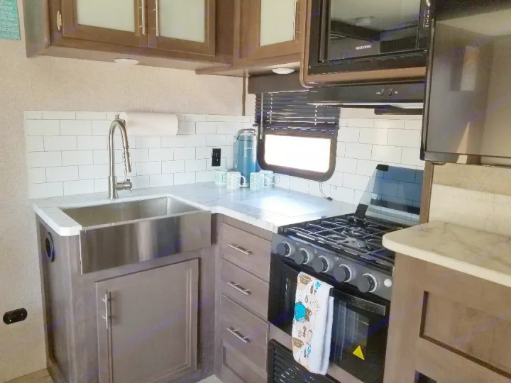 Modern RV rental kitchen featuring a stainless steel sink, subway tile backsplash, stove, and microwave.. Dutchmen Coleman 2021