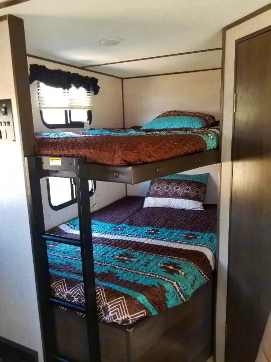 Inside an RV rental: two bunk beds with colorful Southwestern-style bedding, a ladder, and a window for comfortable sleeping.. Dutchmen Coleman 2021
