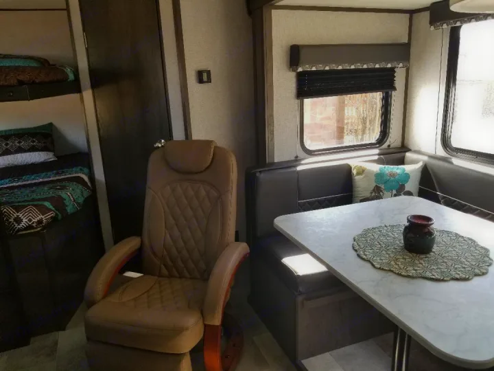 Spacious RV rental interior: bunk beds, a comfy recliner, and a bright dinette with built-in seating and large windows.. Dutchmen Coleman 2021