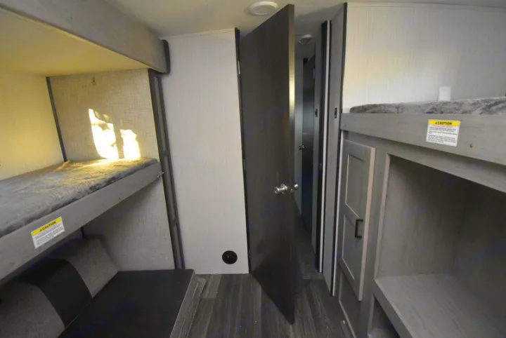 Bright RV rental interior showcases bunk beds, one with lower seating & sunlit wall, the other with storage. Door to another room.. Other M-3385 2020