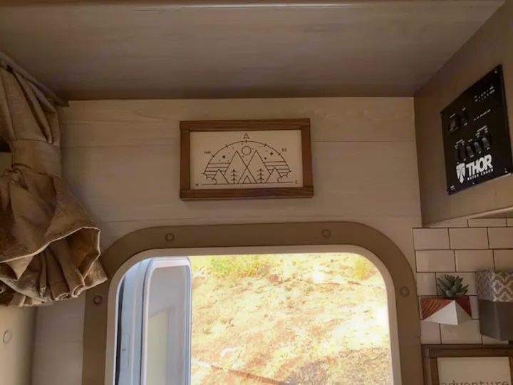 Cozy RV rental interior featuring nature art, a THOR control panel, and a bright window view to a sunny landscape.. Thor Four Winds 2021