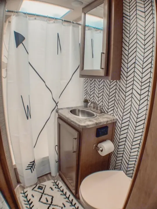 Step inside this modern RV rental bathroom: features a compass shower curtain, compact vanity with sink, toilet, and stylish chevron decor.. Thor Four Winds 2021