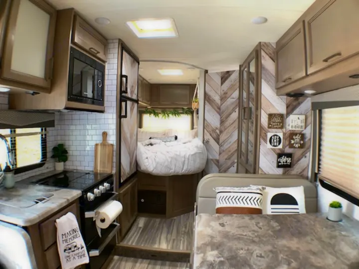Stylish RV rental interior shows kitchen, dining, & cozy bed. Herringbone accents & modern decor.. Thor Four Winds 2021