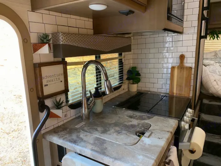 Modern RV rental kitchen featuring a white subway tile backsplash, sink, and stovetop.. Thor Four Winds 2021