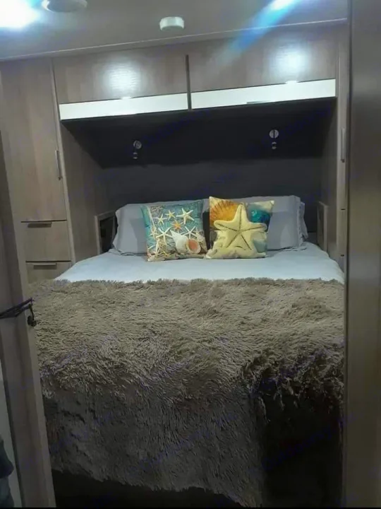 Cozy RV rental bedroom featuring a plush bed with seashell pillows and built-in storage. Ideal for comfortable travel.. Grand Design Imagine 23 BHE 2021