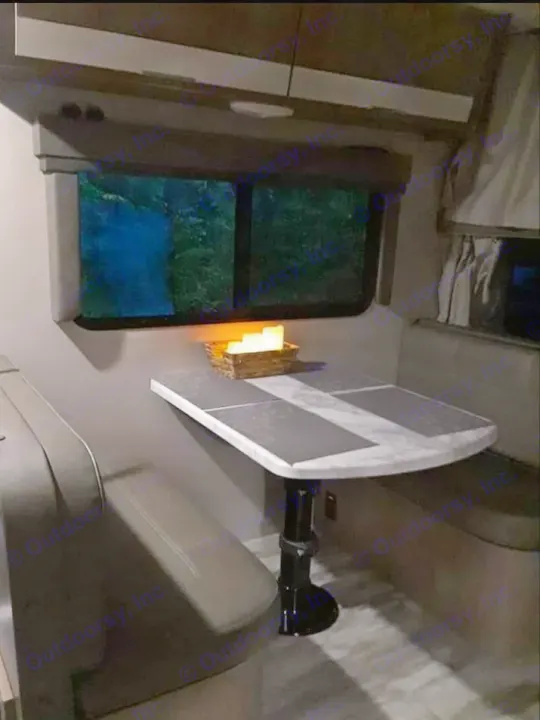 Cozy rv rental dinette with padded benches, a table, glowing candles, and a window looking out at a dim forest with a blue glow.. Grand Design Imagine 23 BHE 2021