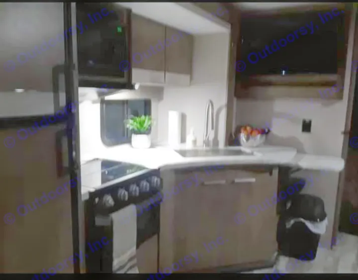 Cozy RV rental kitchen at night, featuring a microwave, stove, sink, and countertop. Perfect for camping adventures!. Grand Design Imagine 23 BHE 2021