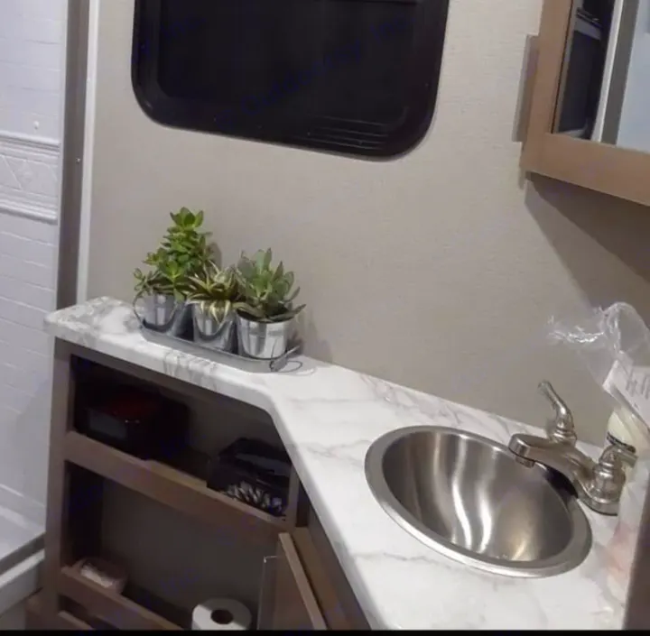 This RV rental bathroom features a compact vanity with a stainless steel sink, built-in storage, and decorative plants.. Grand Design Imagine 23 BHE 2021