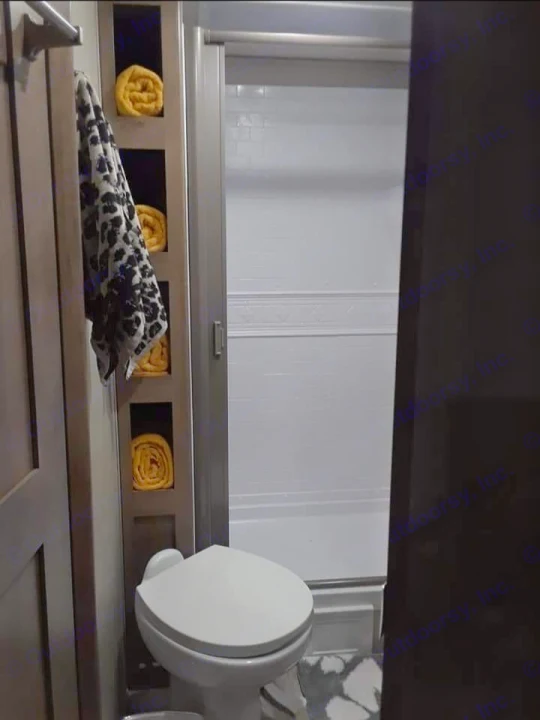 Inside an RV rental bathroom: toilet, shower stall, and neat towel storage with yellow and patterned towels. Efficient design.. Grand Design Imagine 23 BHE 2021