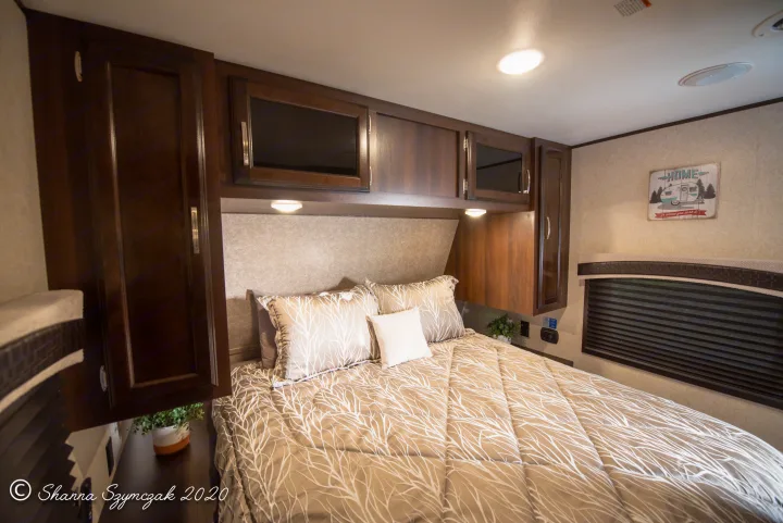 Explore this inviting RV rental bedroom. It features a patterned bed, wood cabinets, lighting, and a window.. Jayco Bunkhouse 2020