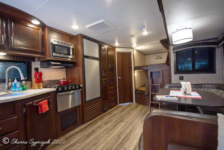 Modern RV rental interior: kitchen, dining, and bunk beds with rich wood finishes.. Jayco Bunkhouse 2020