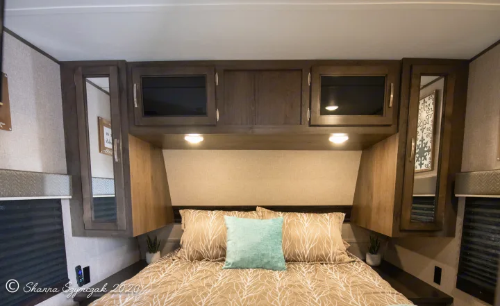 Comfortable RV rental bedroom with patterned bed, teal pillow, and dark wood cabinets, perfect for a cozy interior.. Jayco Jay Flight 2020