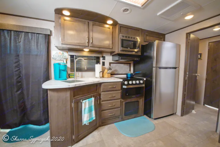 Modern RV rental kitchen with dark wood cabinets, stainless steel appliances, and a "Camping Zone" sign, offering all home comforts.. Jayco Jay Flight 2020