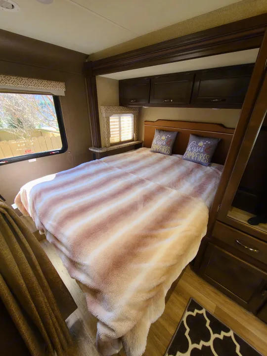 Cozy RV rental bedroom with striped blanket and "kisses & campfires" pillows. Perfect for travel!. Thor Freedom Elite 2019