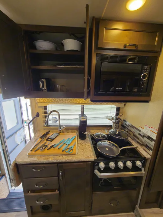 Compact, full-featured RV rental kitchen with microwave, stove, sink, and ample storage for cooking on the go.. Thor Freedom Elite 2019