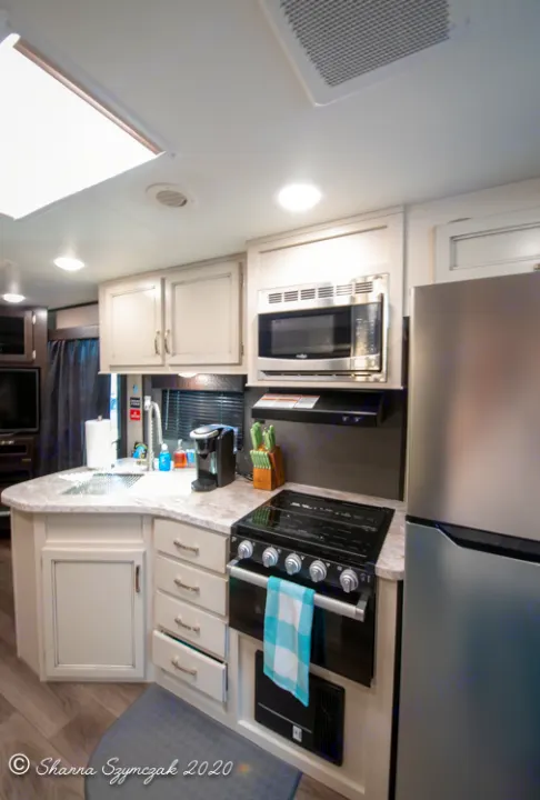 Inside an RV rental: a bright, compact kitchen with a sink, stove, microwave, and stainless steel fridge.. Jayco Jay Flight 2021