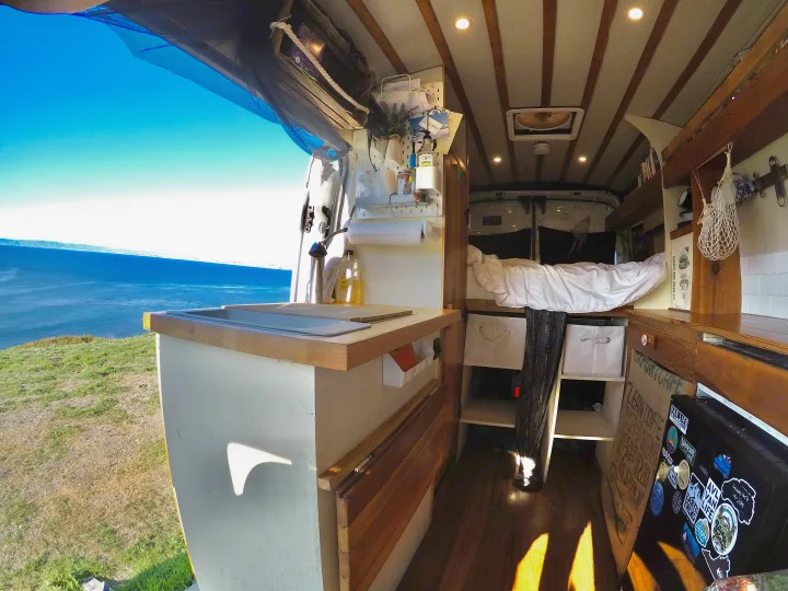 Interior of an RV rental: a cozy camper van with a stunning ocean view from the open door, showcasing the ultimate van life experience.. Ford Transit 2017