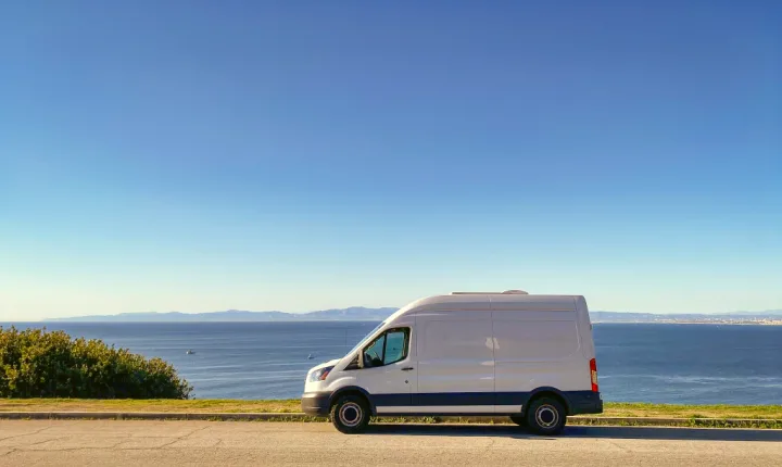 White camper van RV rental parked by a stunning ocean view, ready for your next road trip adventure.. Ford Transit 2017