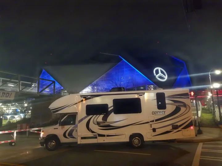 White RV rental parked at night outside Mercedes-Benz Stadium, illuminated in blue. A modern building landmark.. Entegra Coach Other 2021