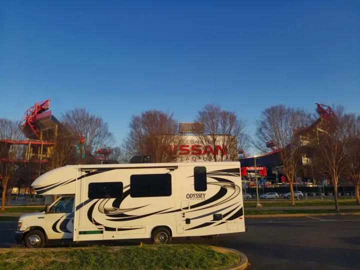 White RV rental (Odyssey Entegra) parked by Nissan Stadium. Clear blue sky over stadium sign and bare trees.. Entegra Coach Other 2021